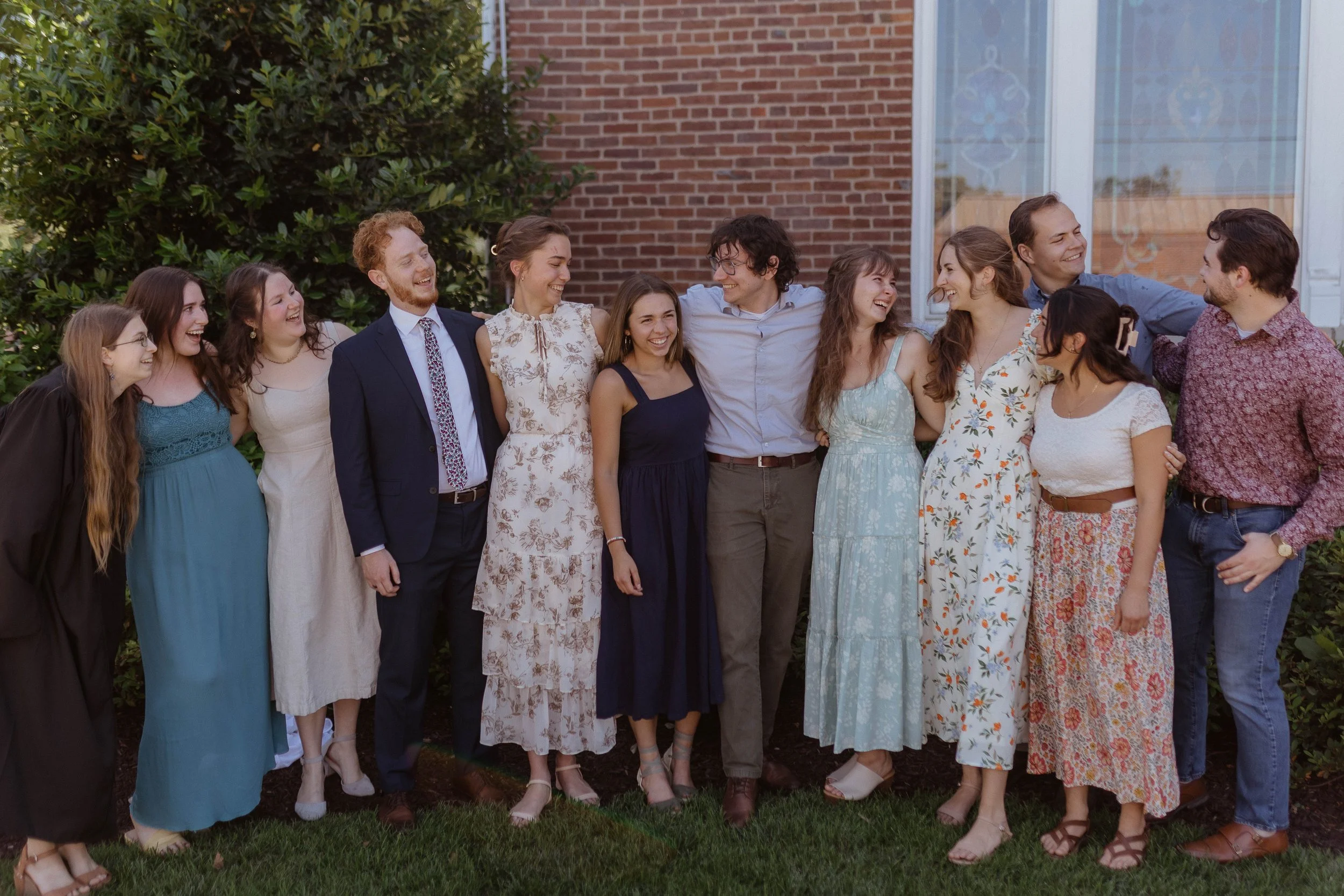 Group of people from a liberal arts school smiling and laughing outdoors, standing in front of a brick house.