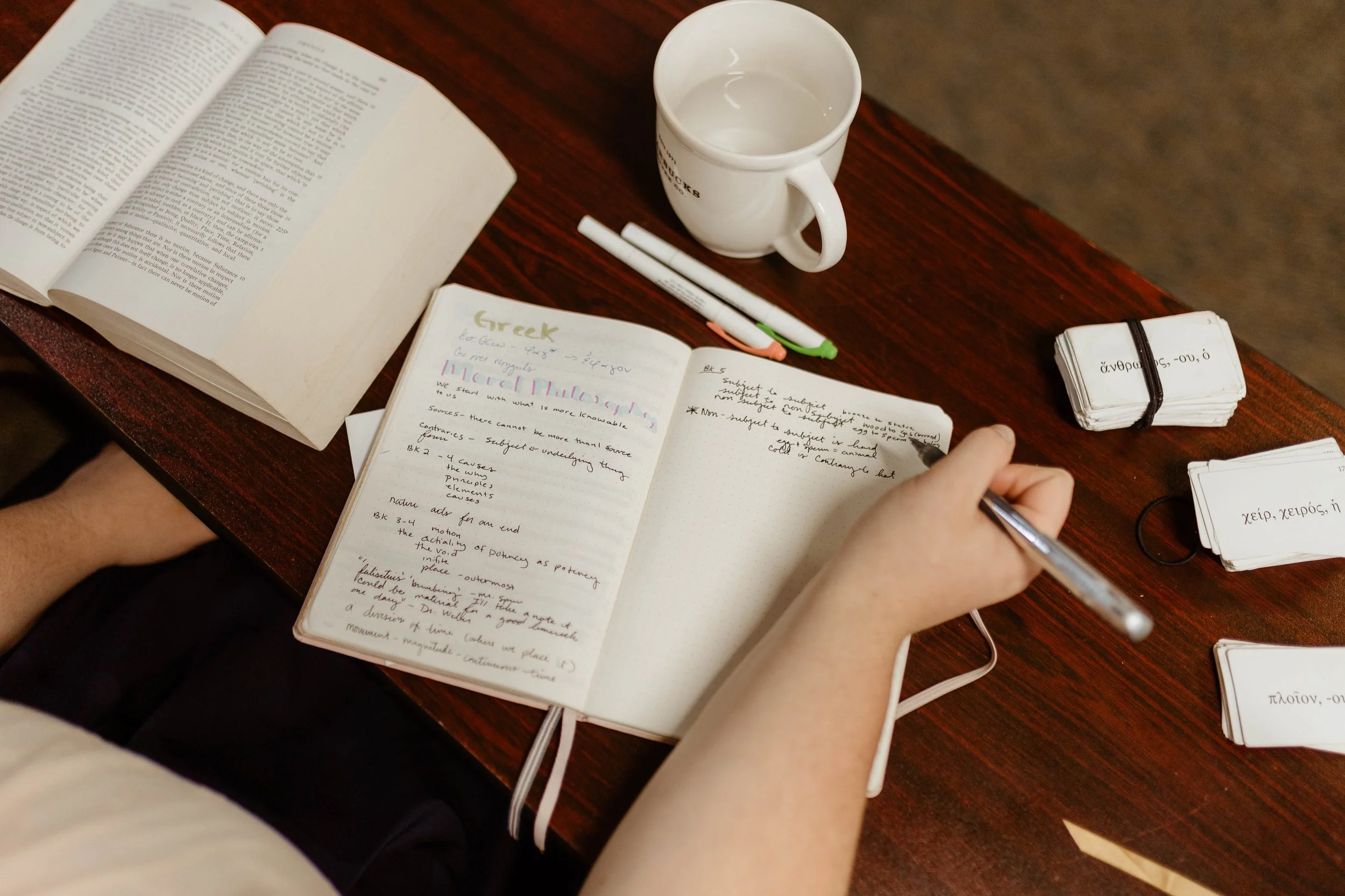 A student is writing notes in a notebook at a small classical school.