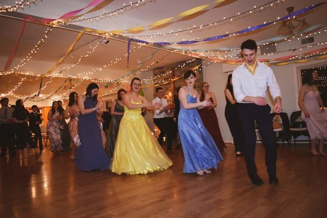 People from a Christian school dancing at a celebration or formal event with colorful streamers and fairy lights overhead.