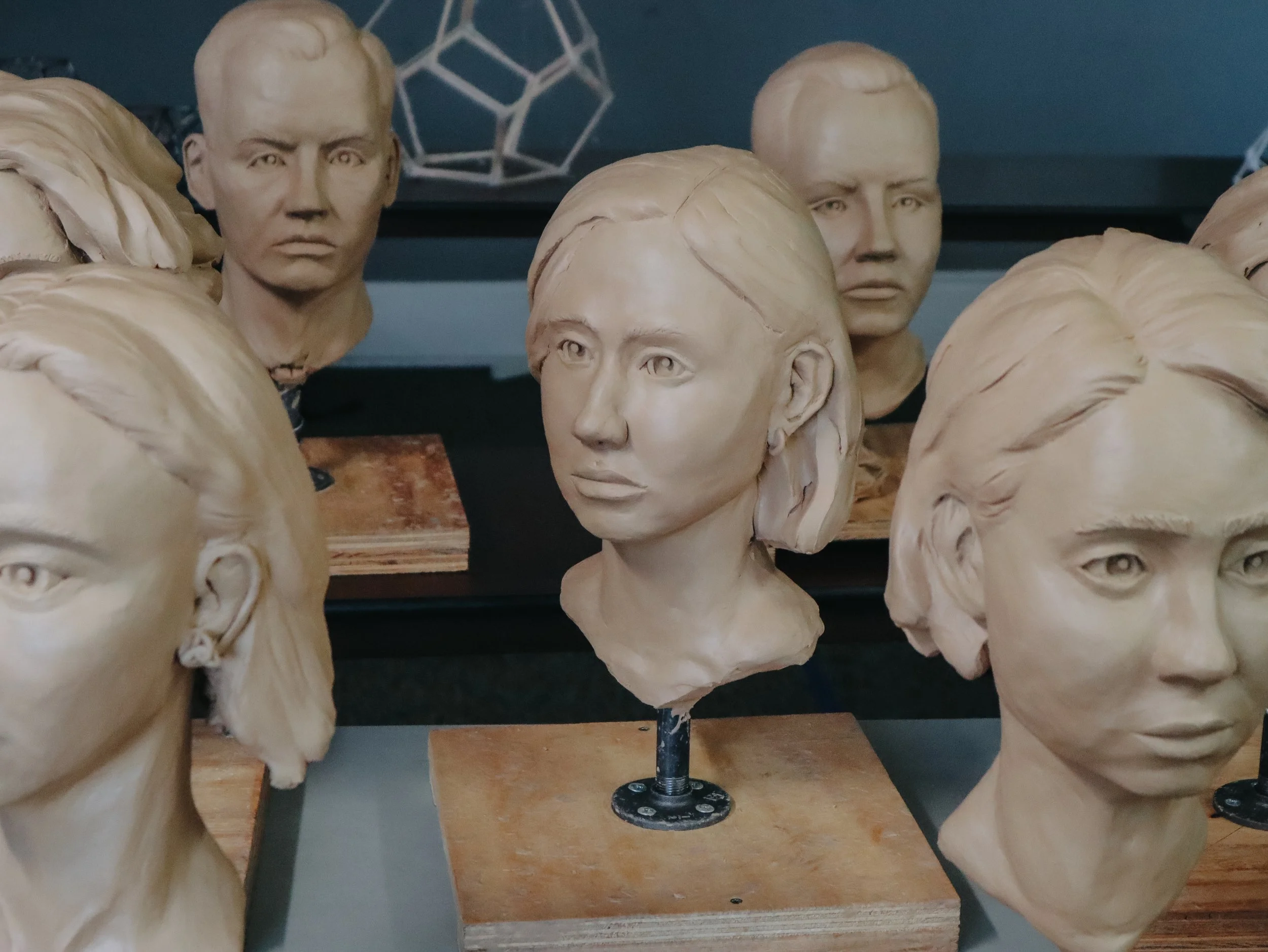 Wooden mannequin heads and busts on display, some with detailed facial features, arranged on shelves and stands, in an artist's studio or workshop.