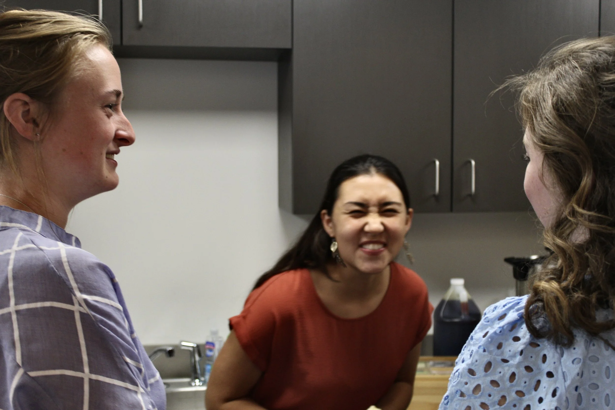 Four women in a kitchen smiling and engaging in conversation.
