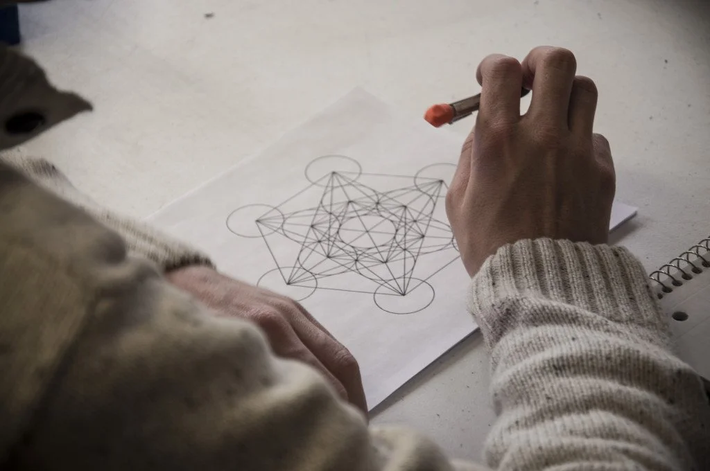 A person drawing a complex geometric diagram consisting of interconnected circles and lines, part of the Quadrivium course.