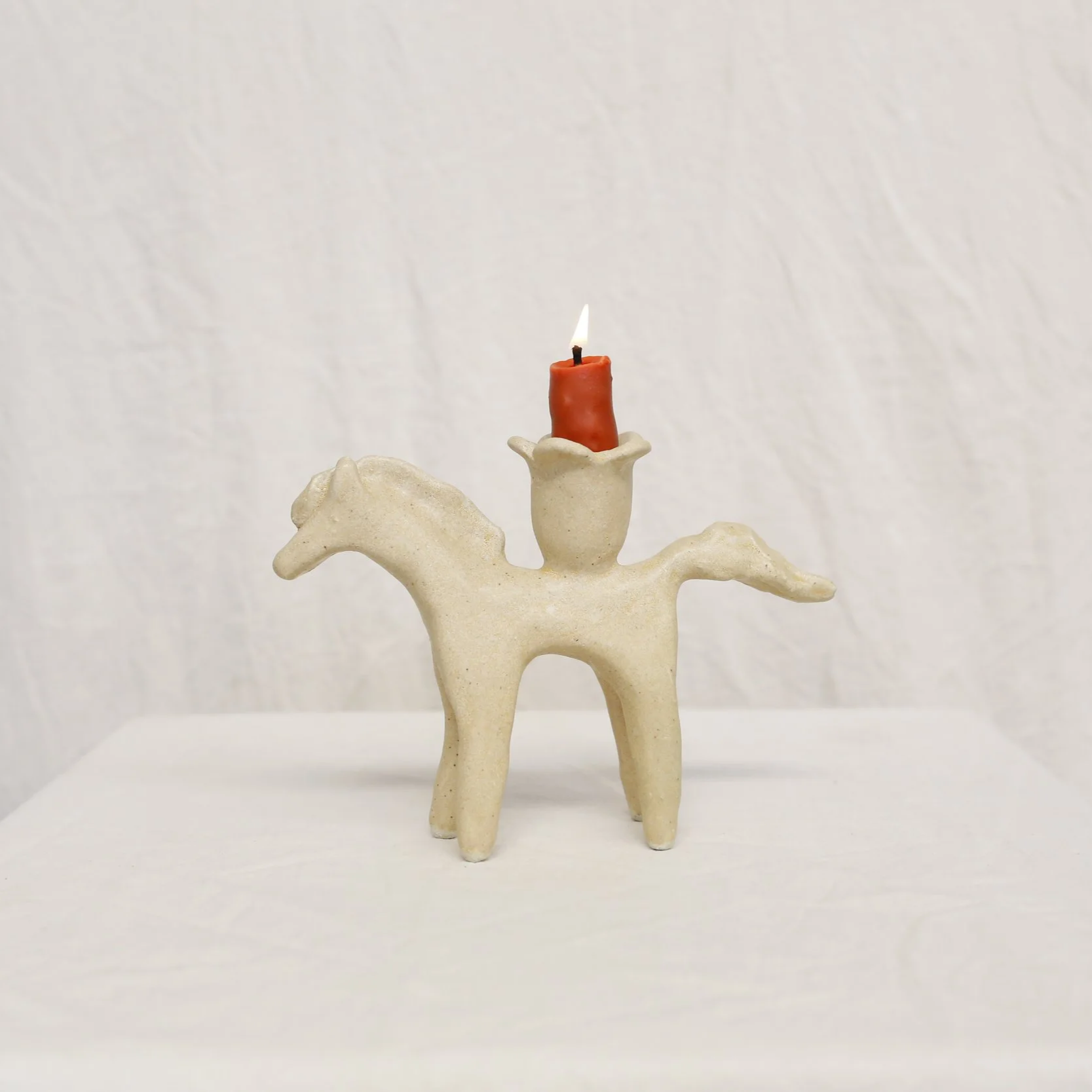 A small sculpture of a horse with a candle holder on its back holding a lit candle.