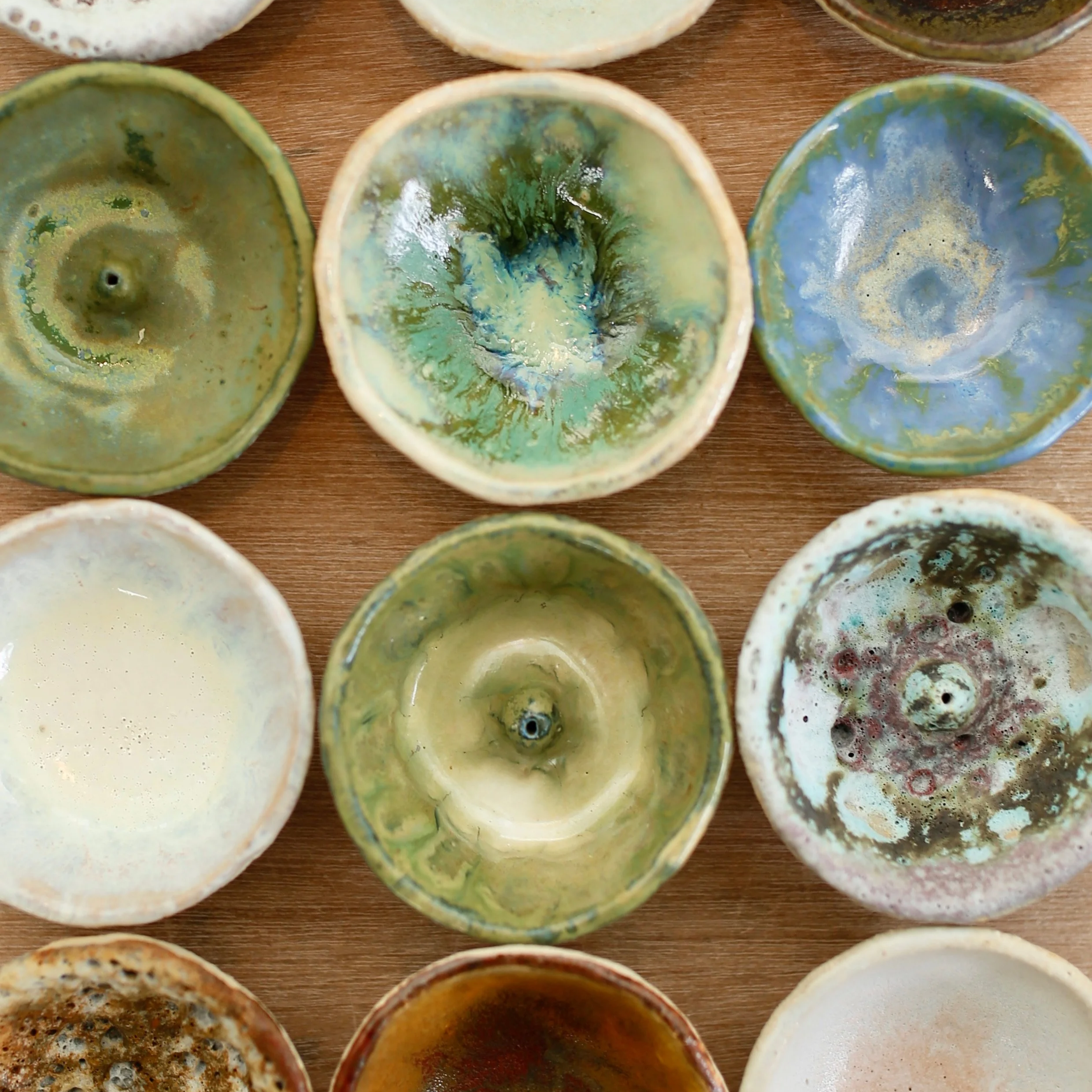 Top-down view of various small ceramic bowls with colorful, abstract glaze patterns, arranged on a wooden surface.