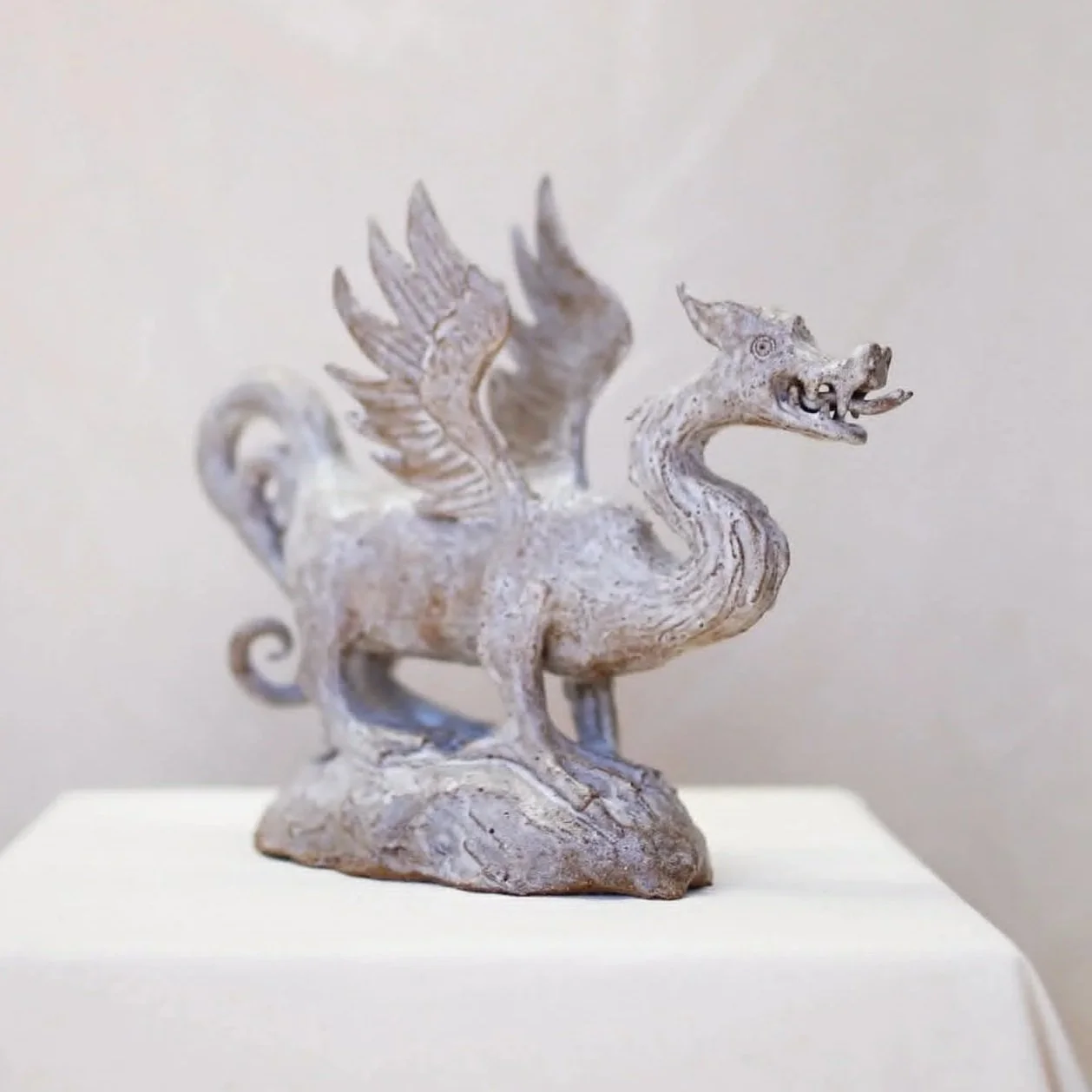 A carved stone sculpture of a mythical creature with a dragon-like head, a serpentine body, wings, and a tail, standing on a rocky base.