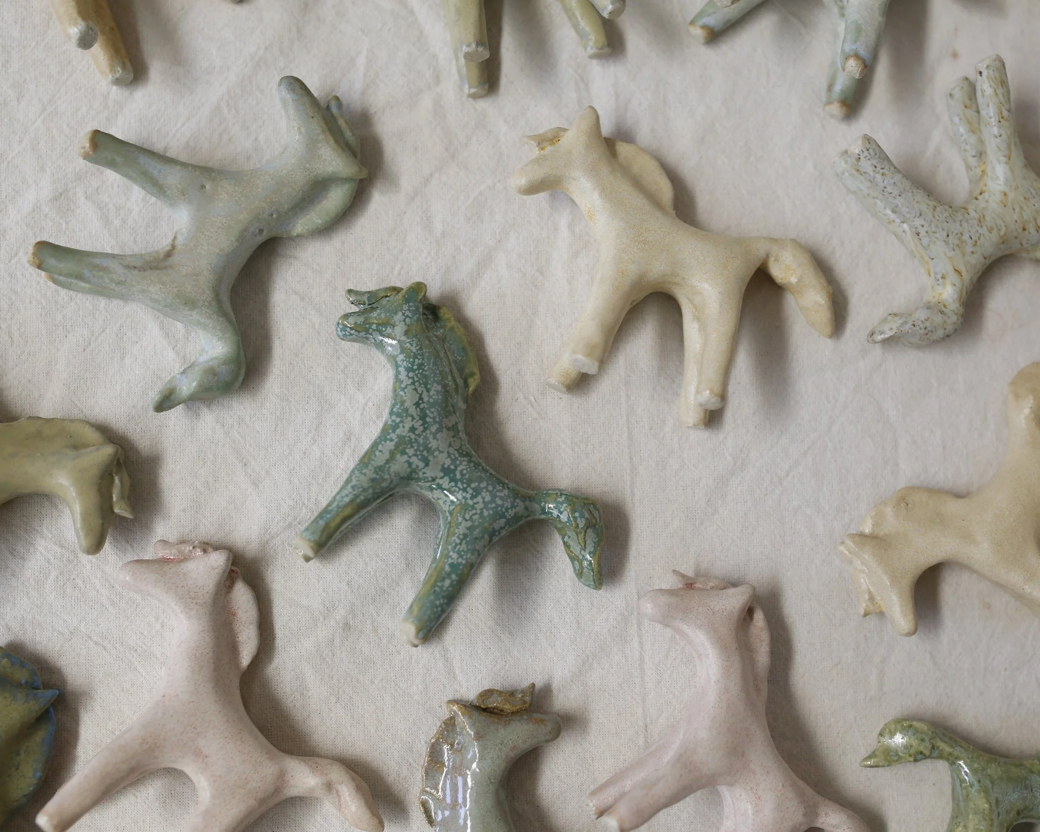 Various ceramic horse figurines in pastel colors scattered on a beige fabric surface.