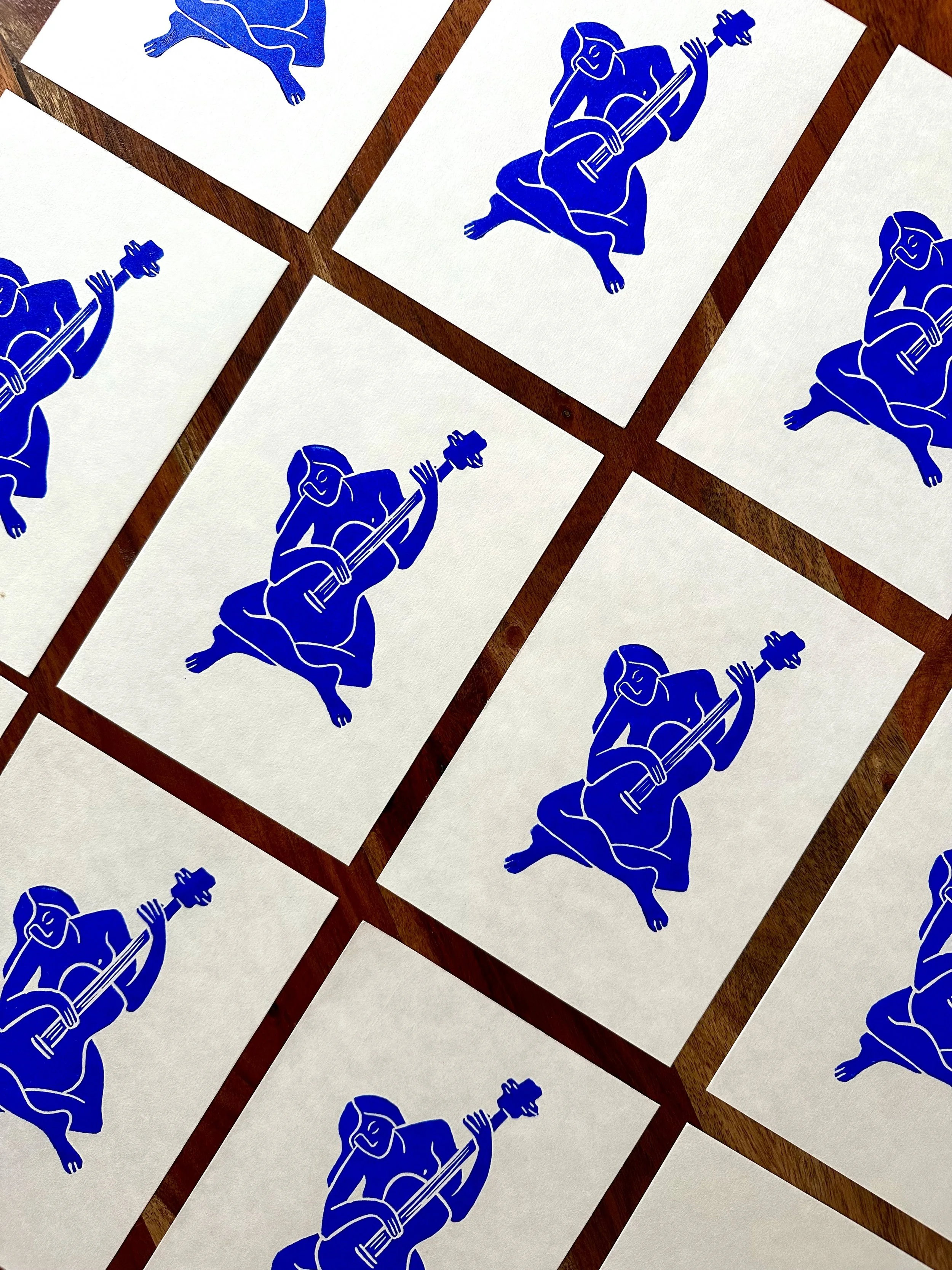 Multiple white cards with blue illustrations of a person kneeling and playing a guitar, arranged on a wooden surface.