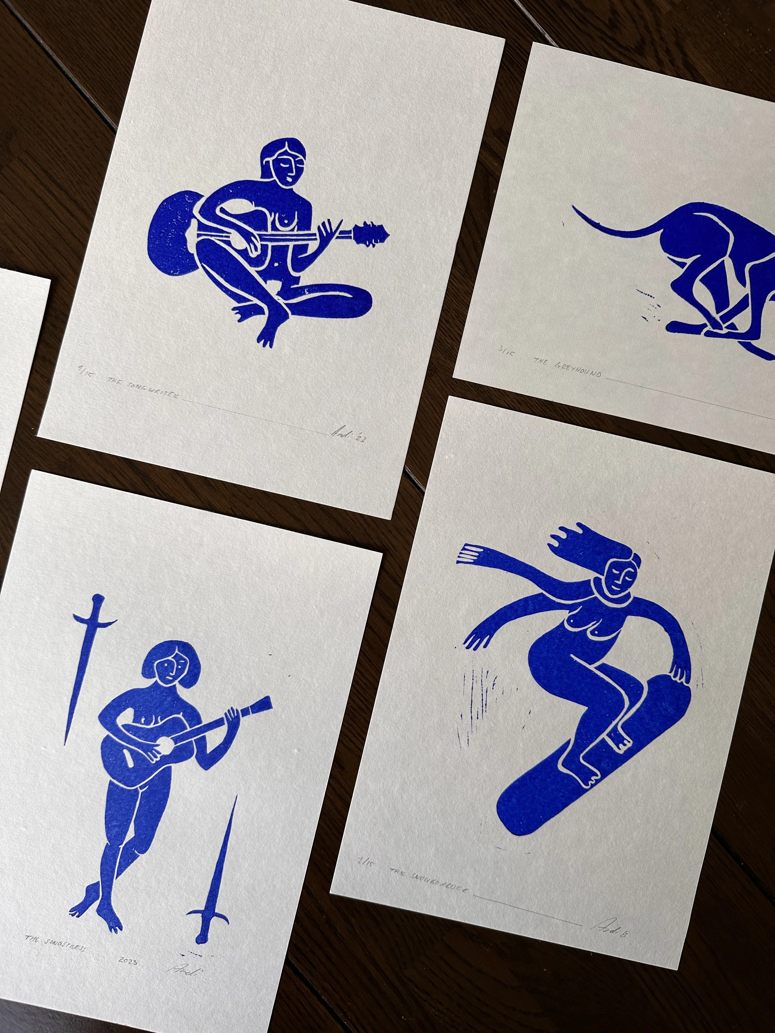 Four blue ink illustrations on white paper, depicting different figures and themes. One shows a seated woman playing a guitar, another is a running dog, the third is a person holding a sword with a spear nearby, and the last is a woman surfing on a w
