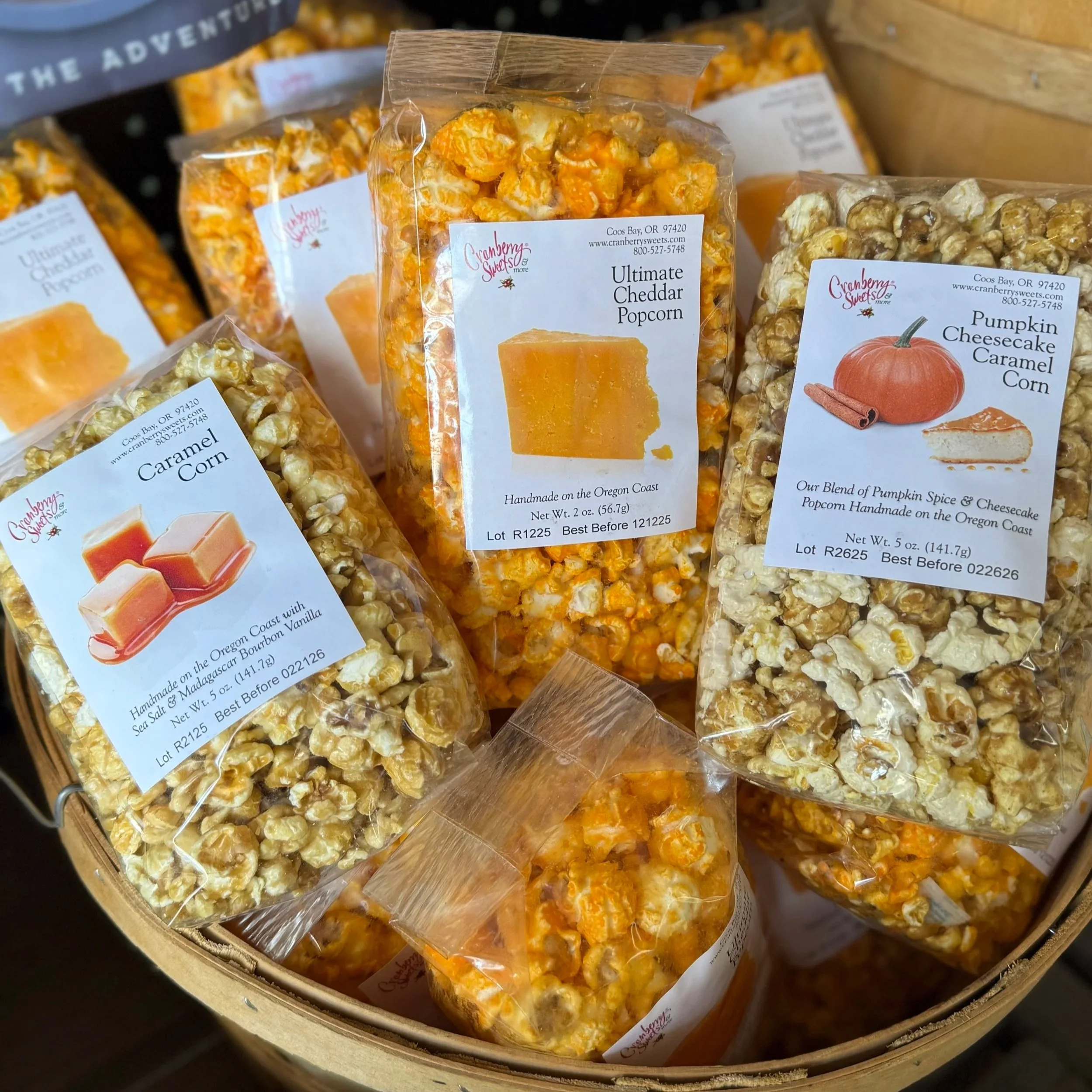 Assorted bags of flavored popcorn, including cheddar, caramel, and pumpkin cheesecake caramel, in a basket.