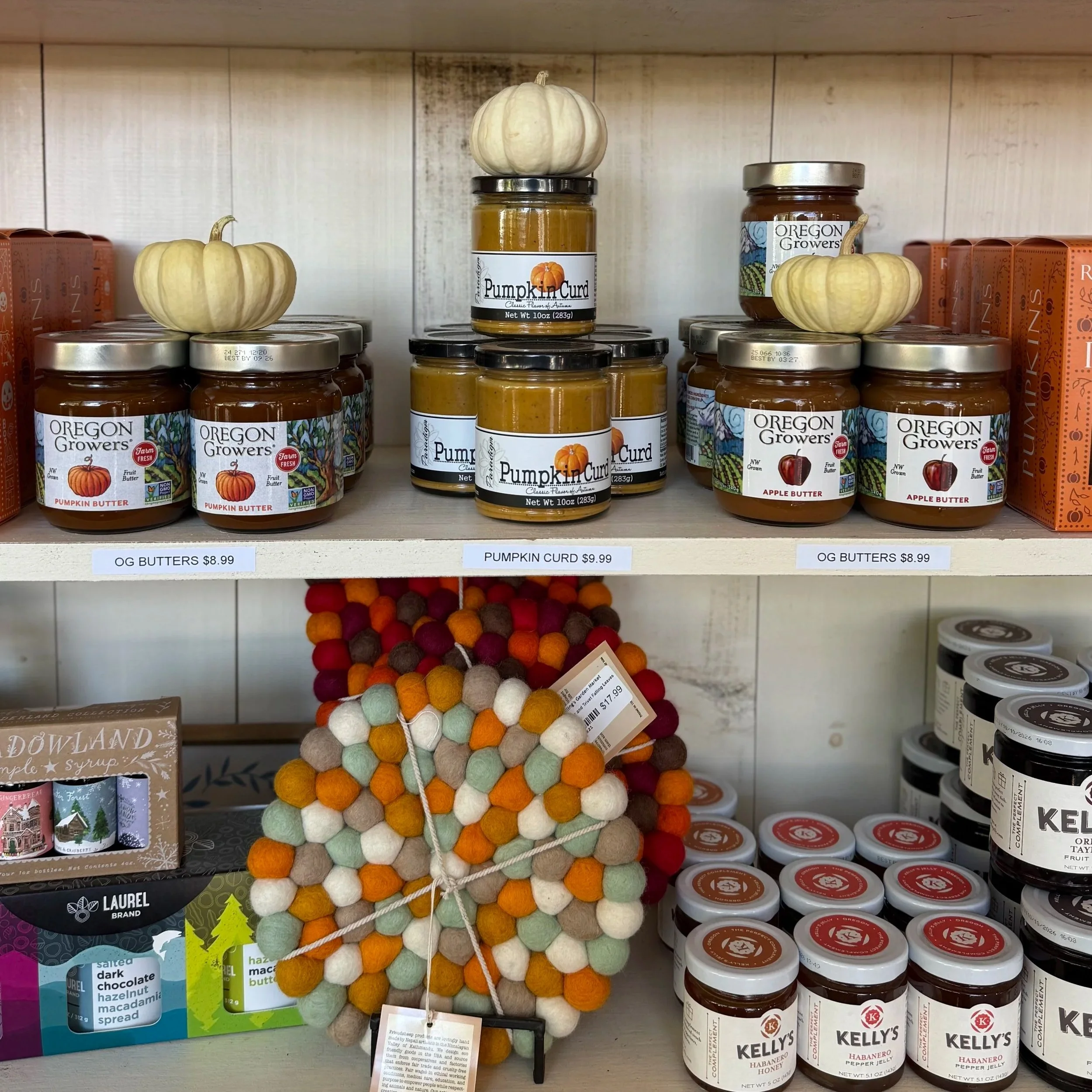 Shelf display of pumpkin and apple butter jars with small decorative gourds on top, priced around $8.99 to $9.99, with felt balls and other products below.