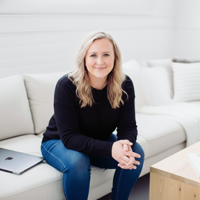 Emily Whitish, Squarespace expert, in a black sweater sitting on a beige sofa in a bright, modern living room with white walls, smiling at the camera.