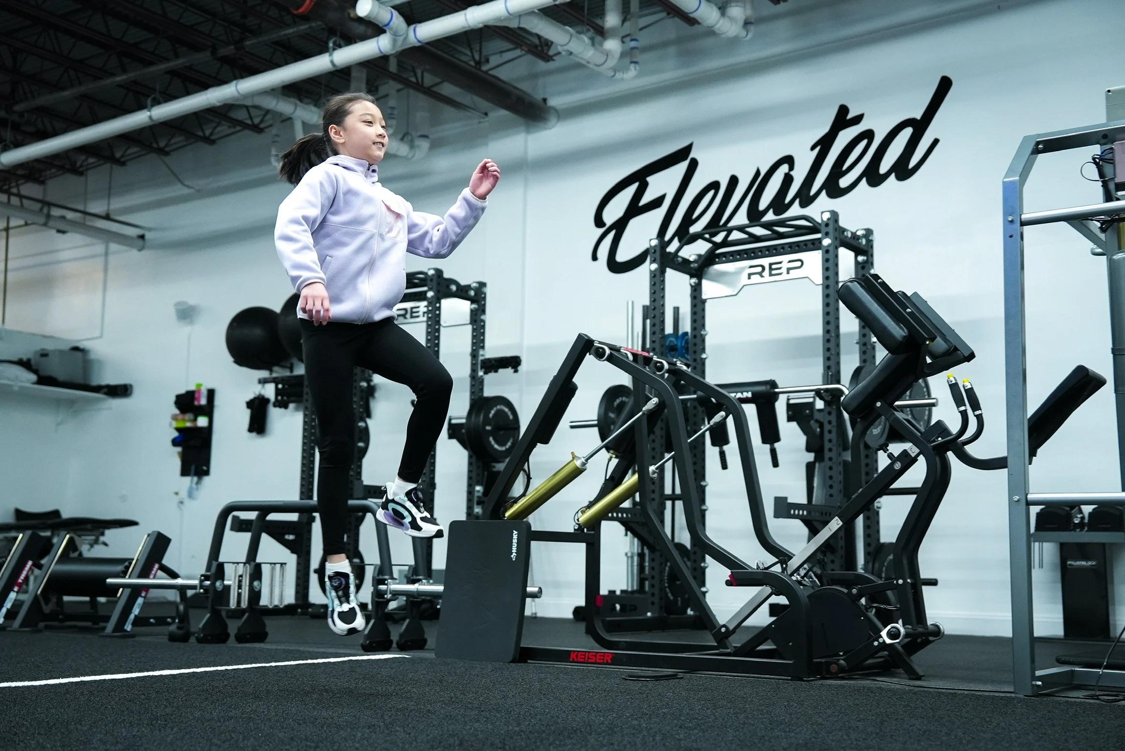 A girl in a white hoodie and black leggings skipping on a stepper in a gym.