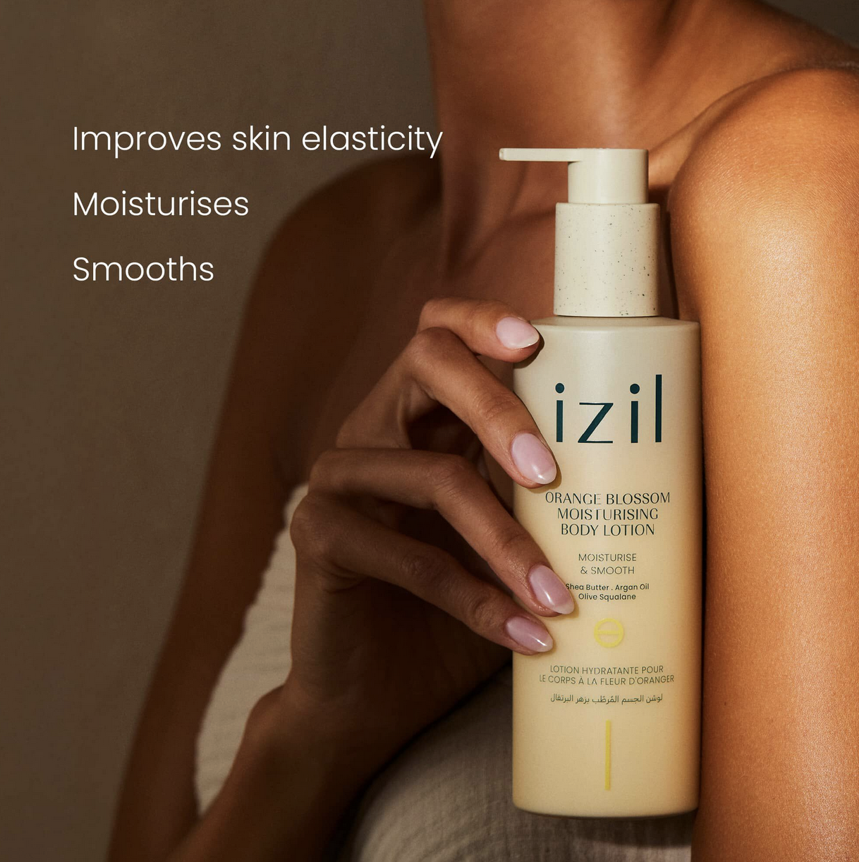 A person holding a bottle of Izil Orange Blossom Moisturizing Body Lotion, which features a pump dispenser, with text indicating benefits such as improving skin elasticity, moisturizing, and smoothing.