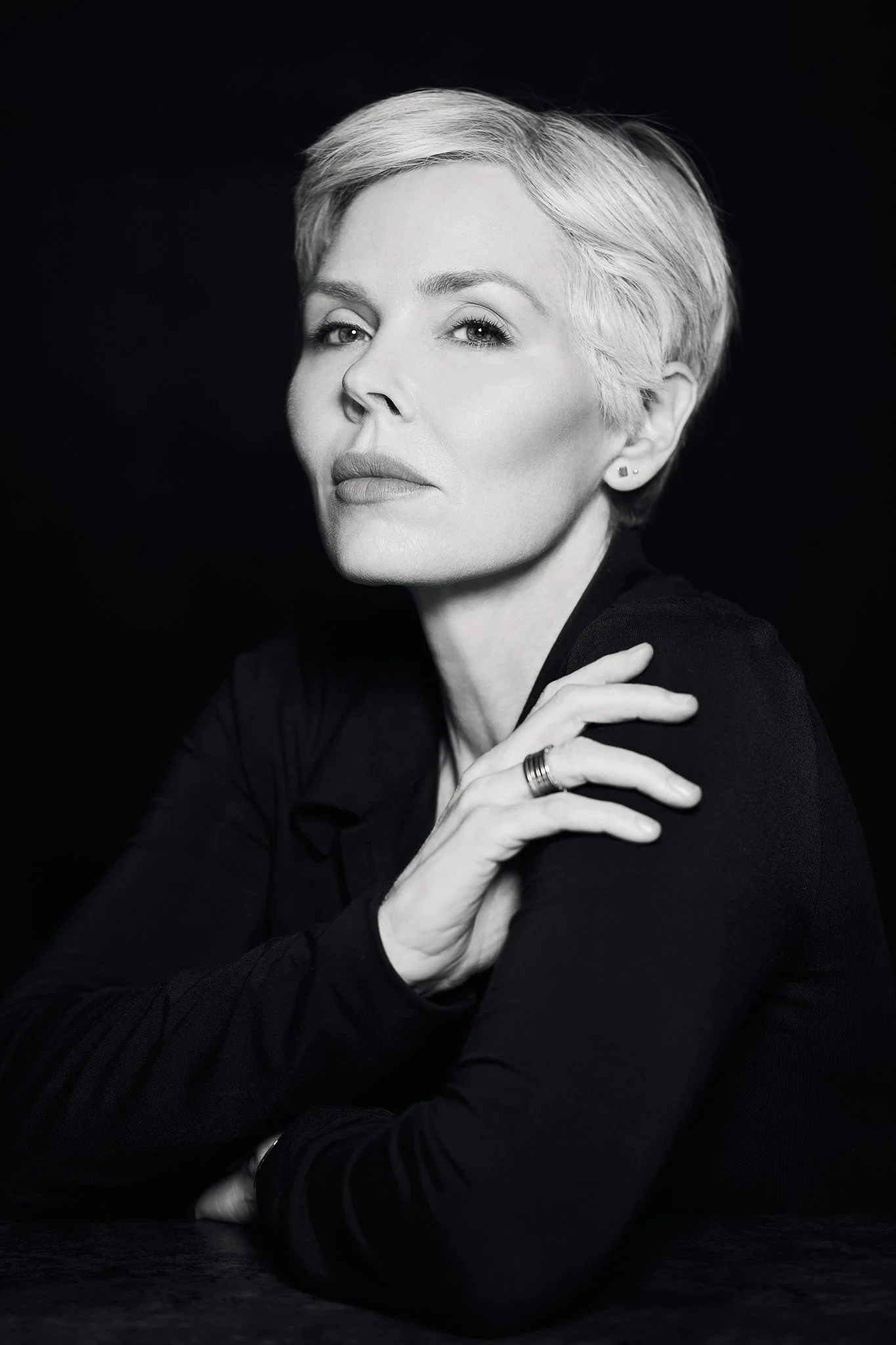 High end personal brand photography in Dubai. Black and white portrait of a woman with short blonde hair, wearing a dark top, looking confidently at the camera, with her hand resting on her shoulder.