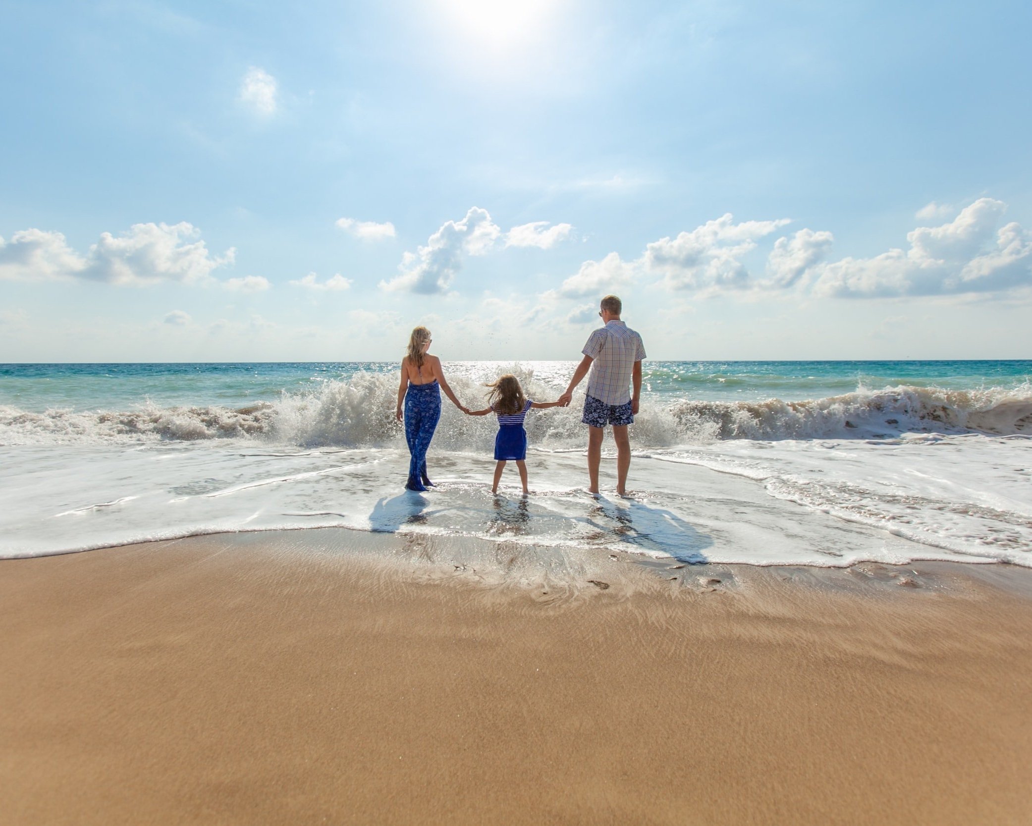 A young family are standing on a beach, they've got their feet in the surf, it represents living in a good lifestyle location with freedom and having success, it represents a guide to saving a deposit on a home.