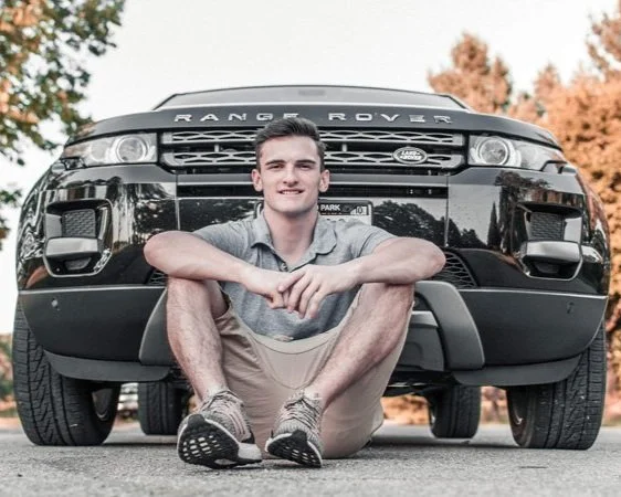 A young man is sitting on the ground in front of his recently purchased Range Rover, it represents the importance of understanding just how much car prices have gone up since the pandemic began.