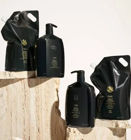 Two black bottles with pump dispensers and two black refill pouches on natural stone surfaces.