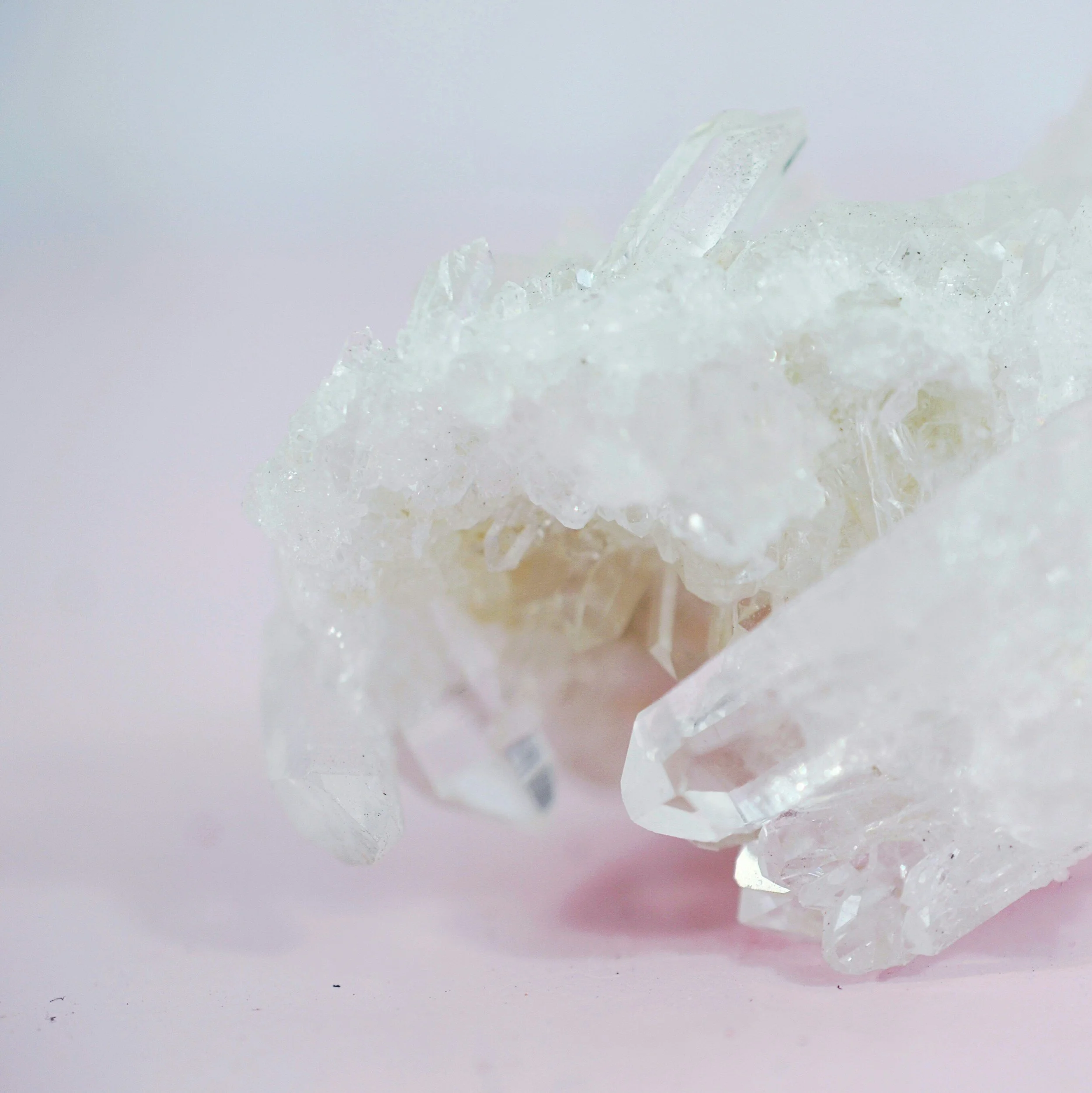 Cluster of clear quartz crystals on a light pink background.