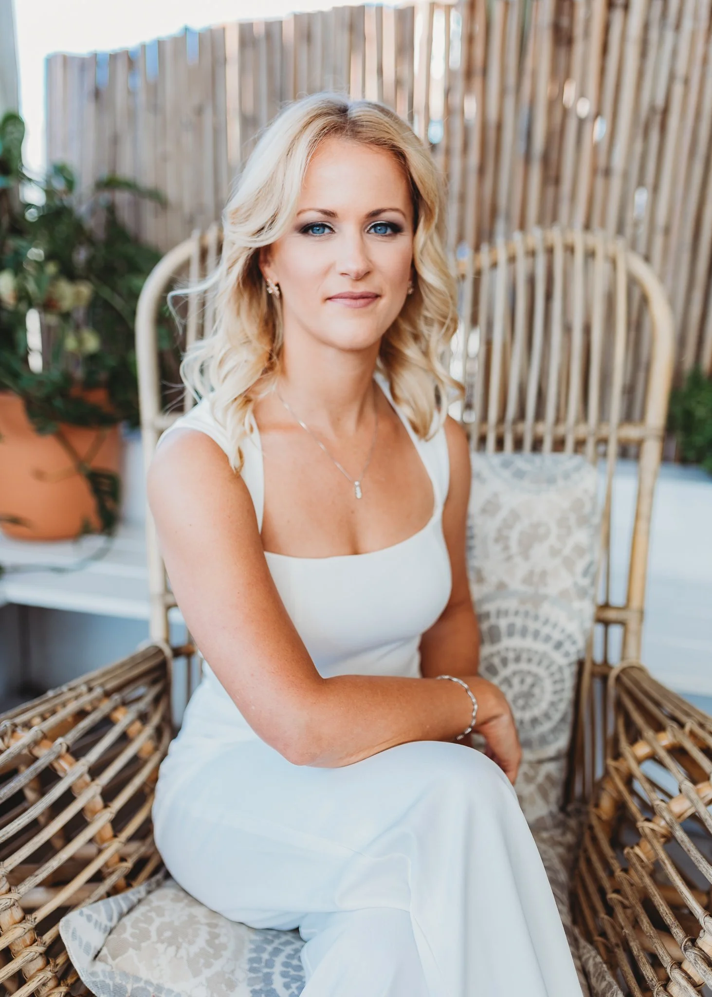 Sage Summer in a white dress sitting on a wicker chair.