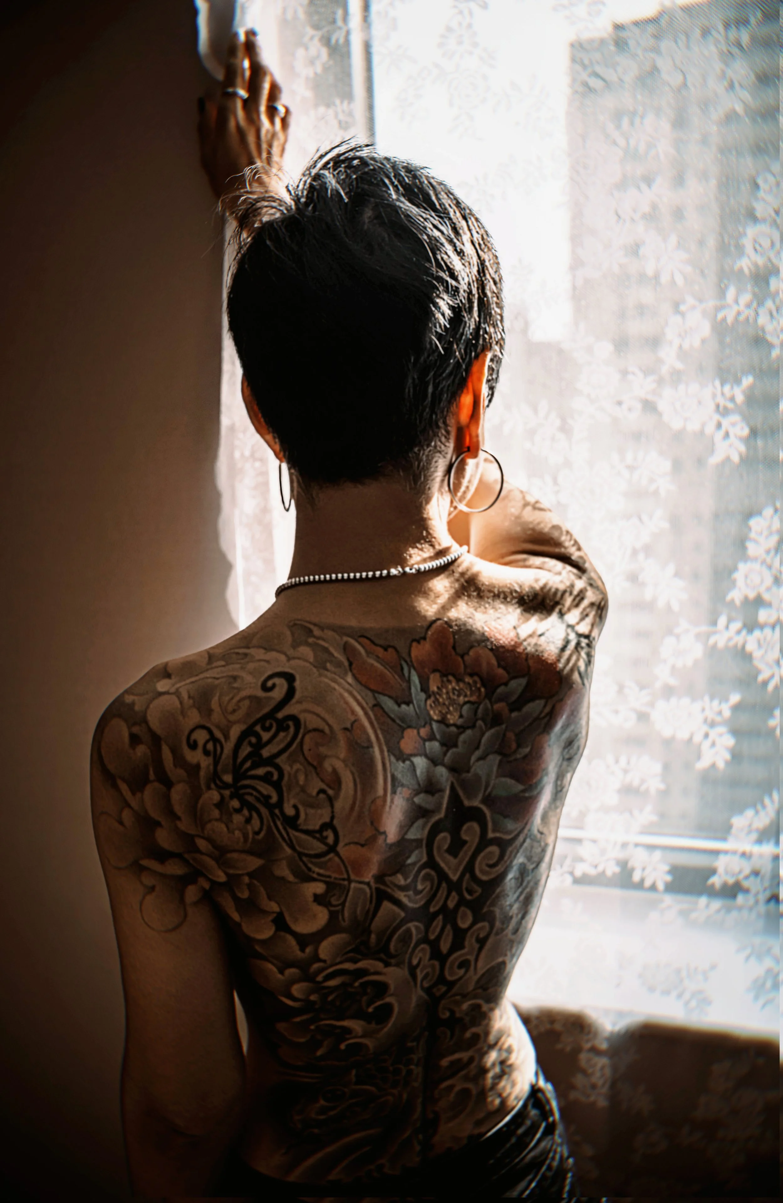 
shannon lu shan documentary & lifestyle family photographer Arnprior , Branding photography. pa woman with short dark hair and multiple tattoos on their shoulder and back, standing by a window 
