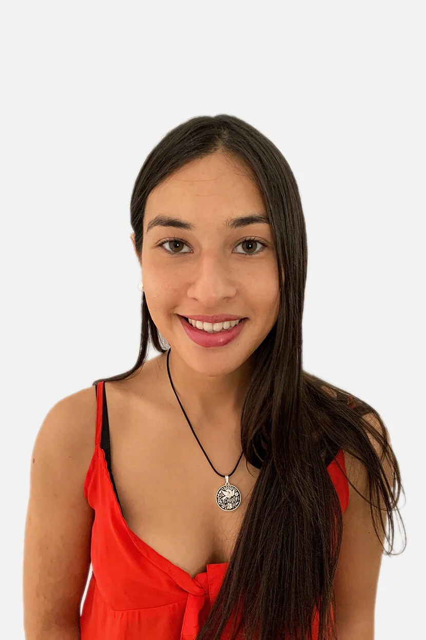 A woman with long dark hair, wearing a red spaghetti strap top and a silver pendant necklace, smiling at the camera, against a plain white background.
