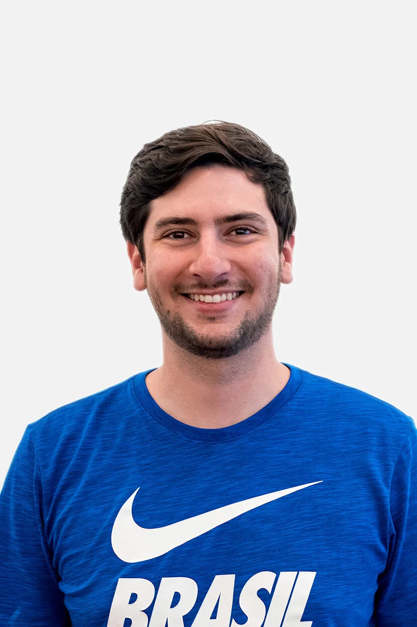 A smiling young man with dark hair and light skin wearing a blue Nike t-shirt with the word 'BRASIL' on it and a white swoosh logo