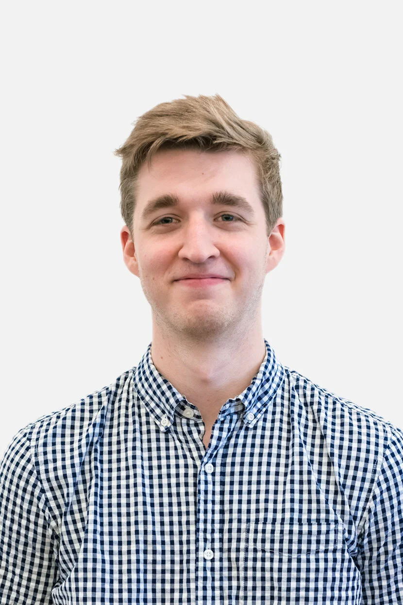 A young man with short, light brown hair, wearing a button-up shirt with a blue and white checkered pattern, smiling lightly facing forward against a plain white background.