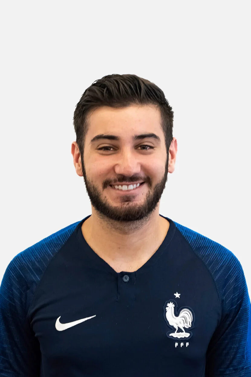 A young man with dark hair and a beard, smiling, wearing a navy blue sports jersey with the French football team logo and Nike logo on the chest.