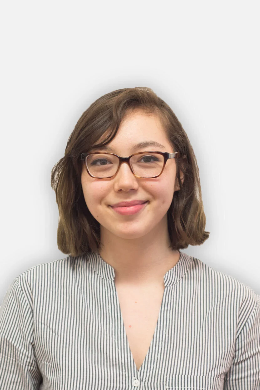 A young woman with shoulder-length brown hair, wearing glasses and a striped shirt, smiling against a plain white background.