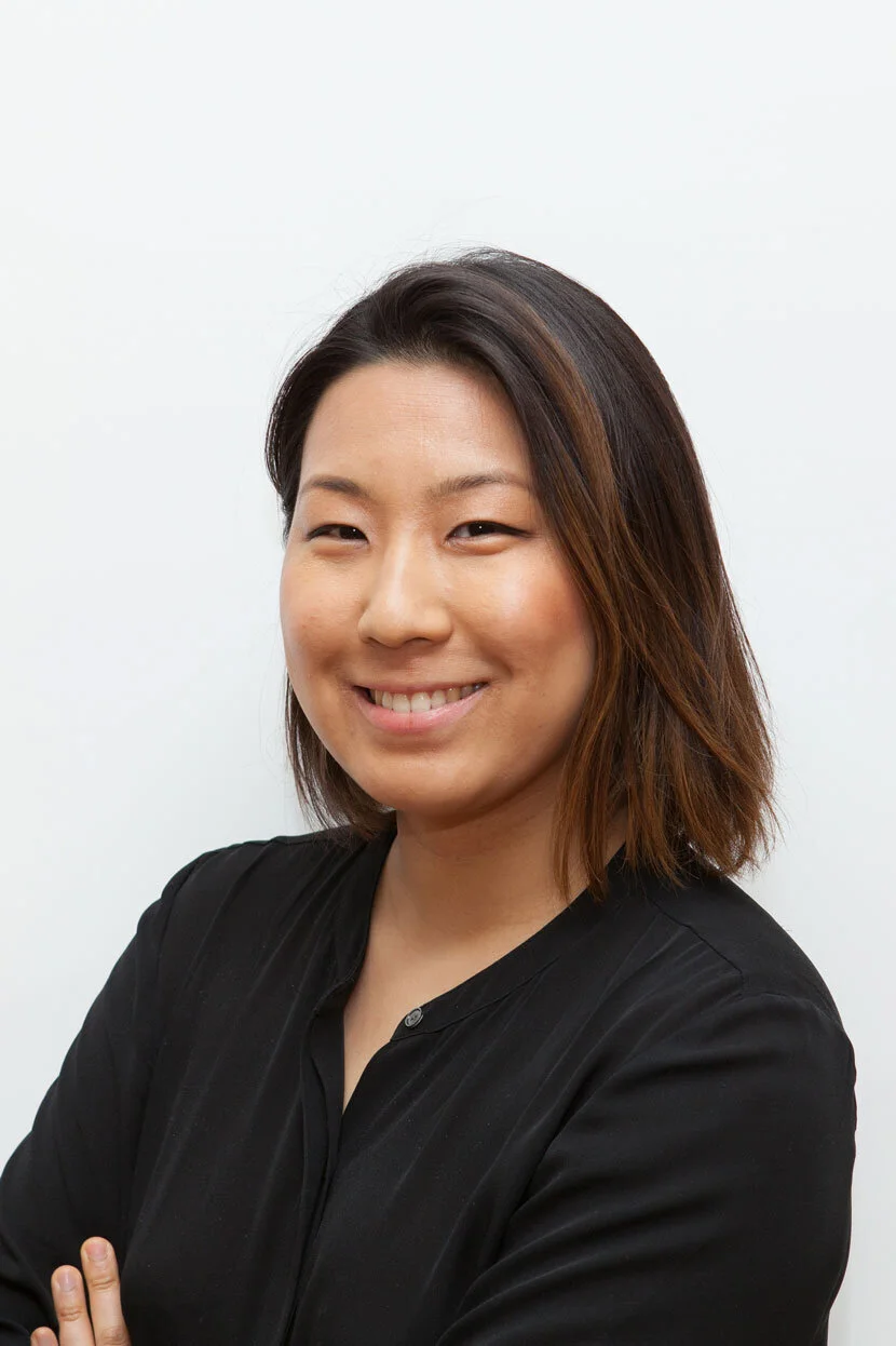 A woman with shoulder-length brown hair, smiling, wearing a black shirt, against a plain white background.