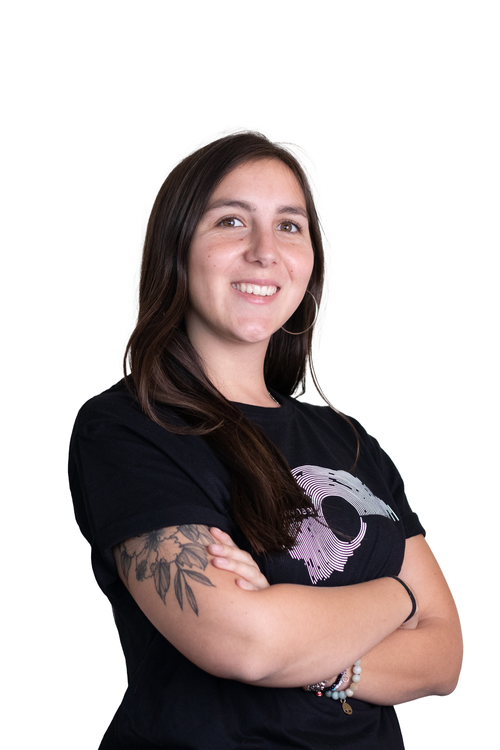 A young woman with long dark hair, wearing a black T-shirt with a graphic design, smiling with arms crossed, standing against a white background.