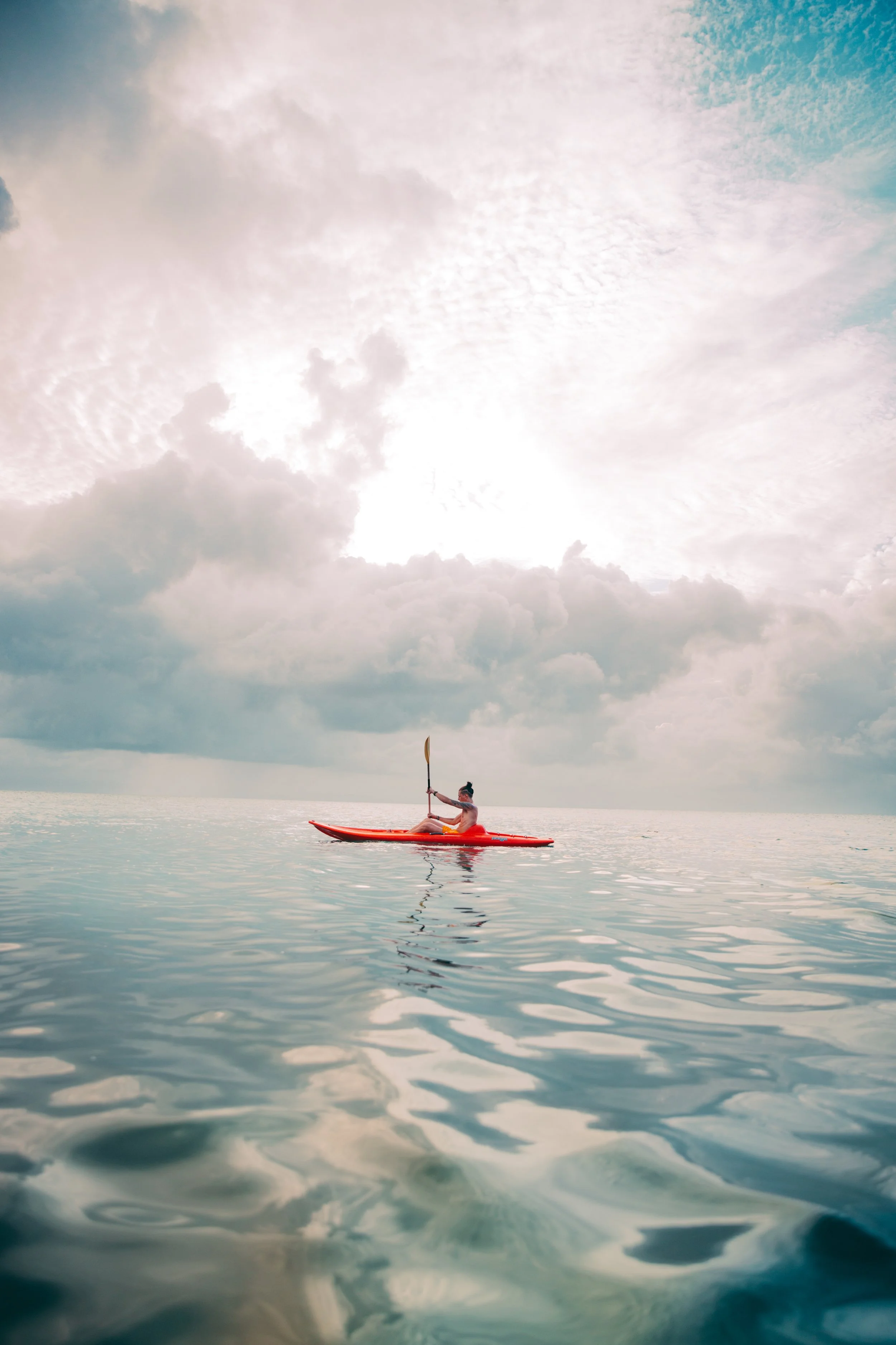 Person kayaking on calm ocean under cloudy sky