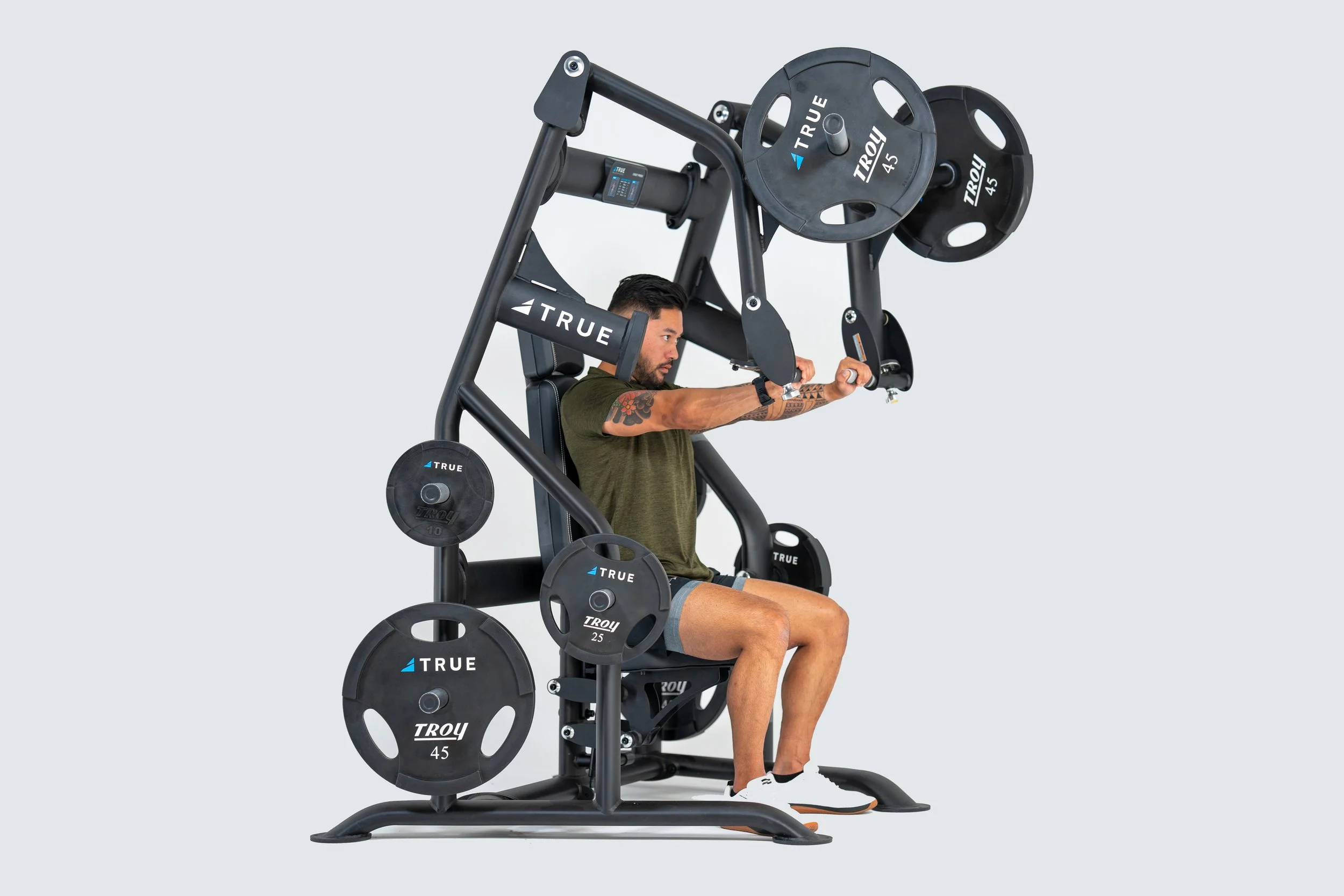 Man using a seated chest press machine with weight plates, wearing green shirt and shorts.
