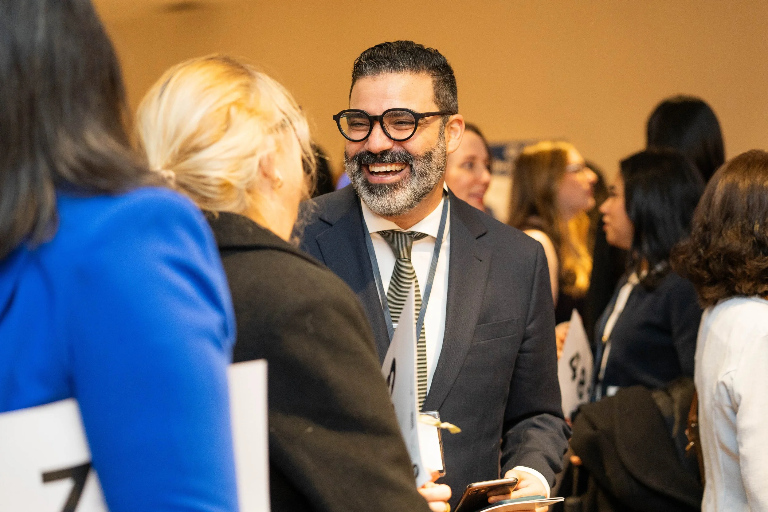 People talking at a professional conference or networking event, smiling and engaging in conversation.