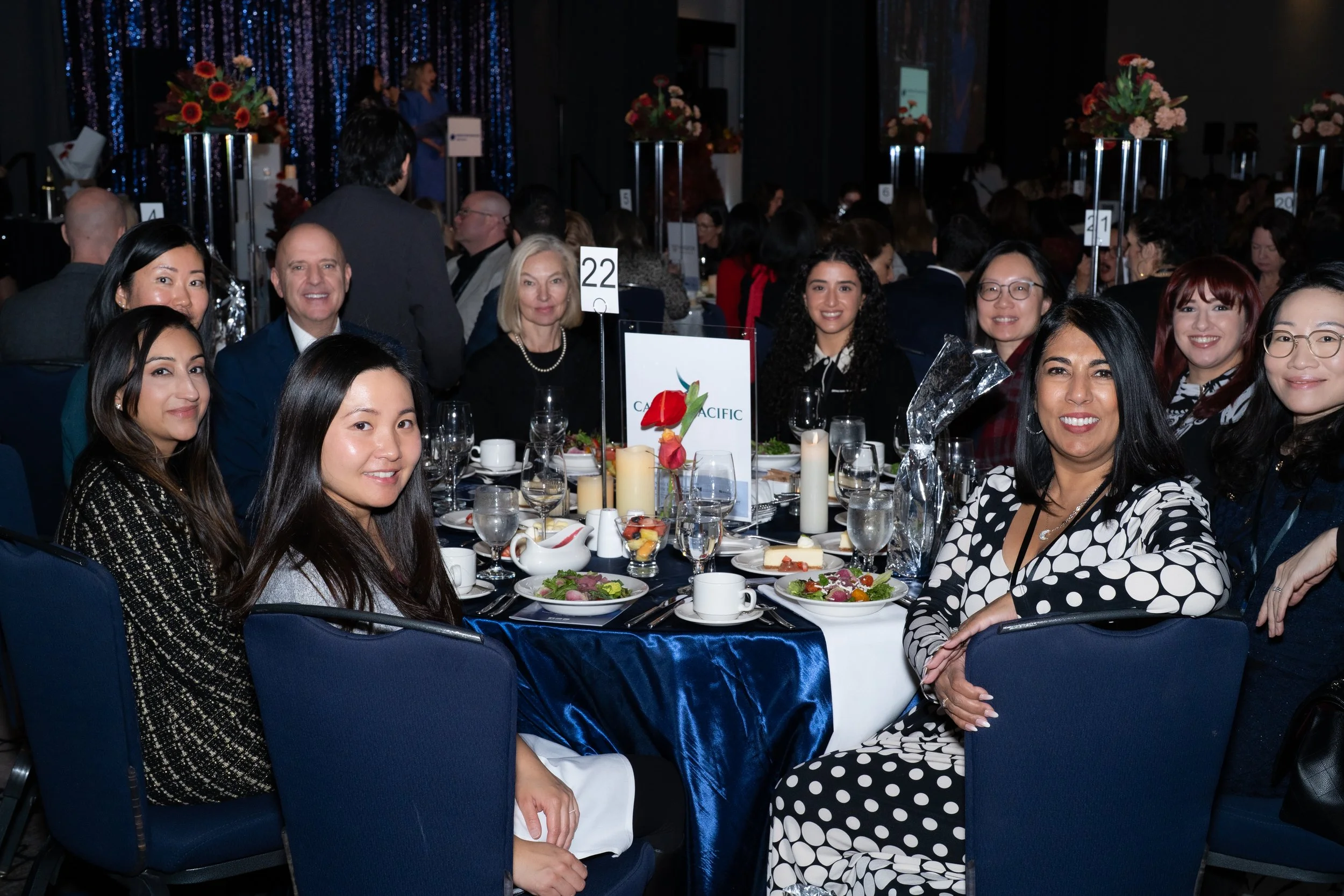 Group of nine people seated at a round banquet table with floral centerpieces and multiple place settings at a formal event or banquet.