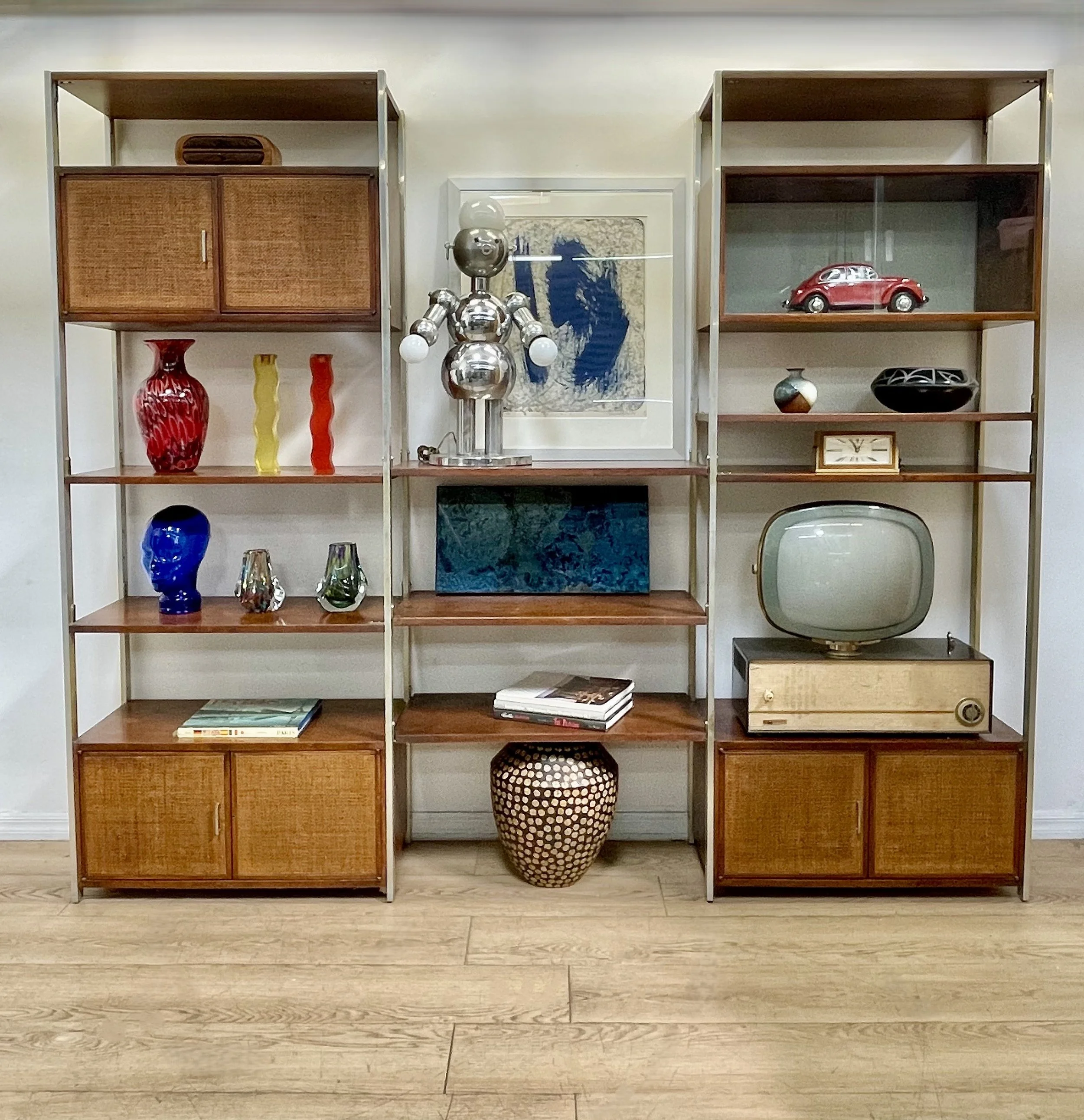 Eclectic vintage interior with plants, antique furniture, decorative paintings, a wicker chair, a turtle figurine, and various knick-knacks arrangement.