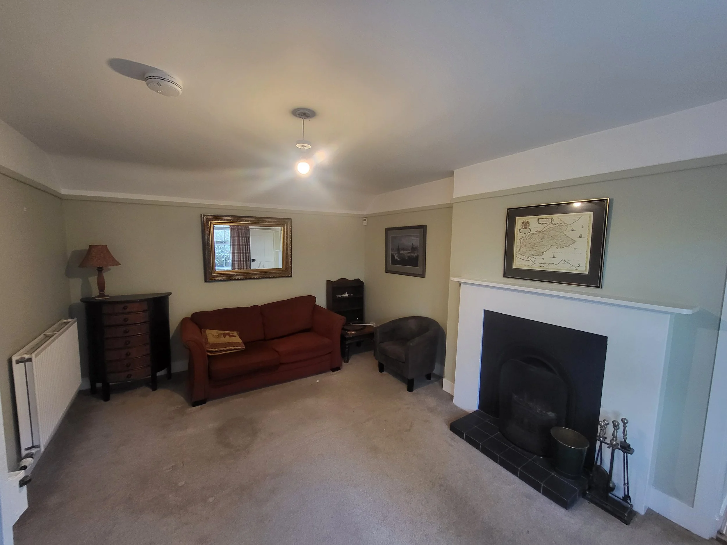 Living room with a red sofa, armchair, fireplace, mirror, framed pictures, and a lamp.