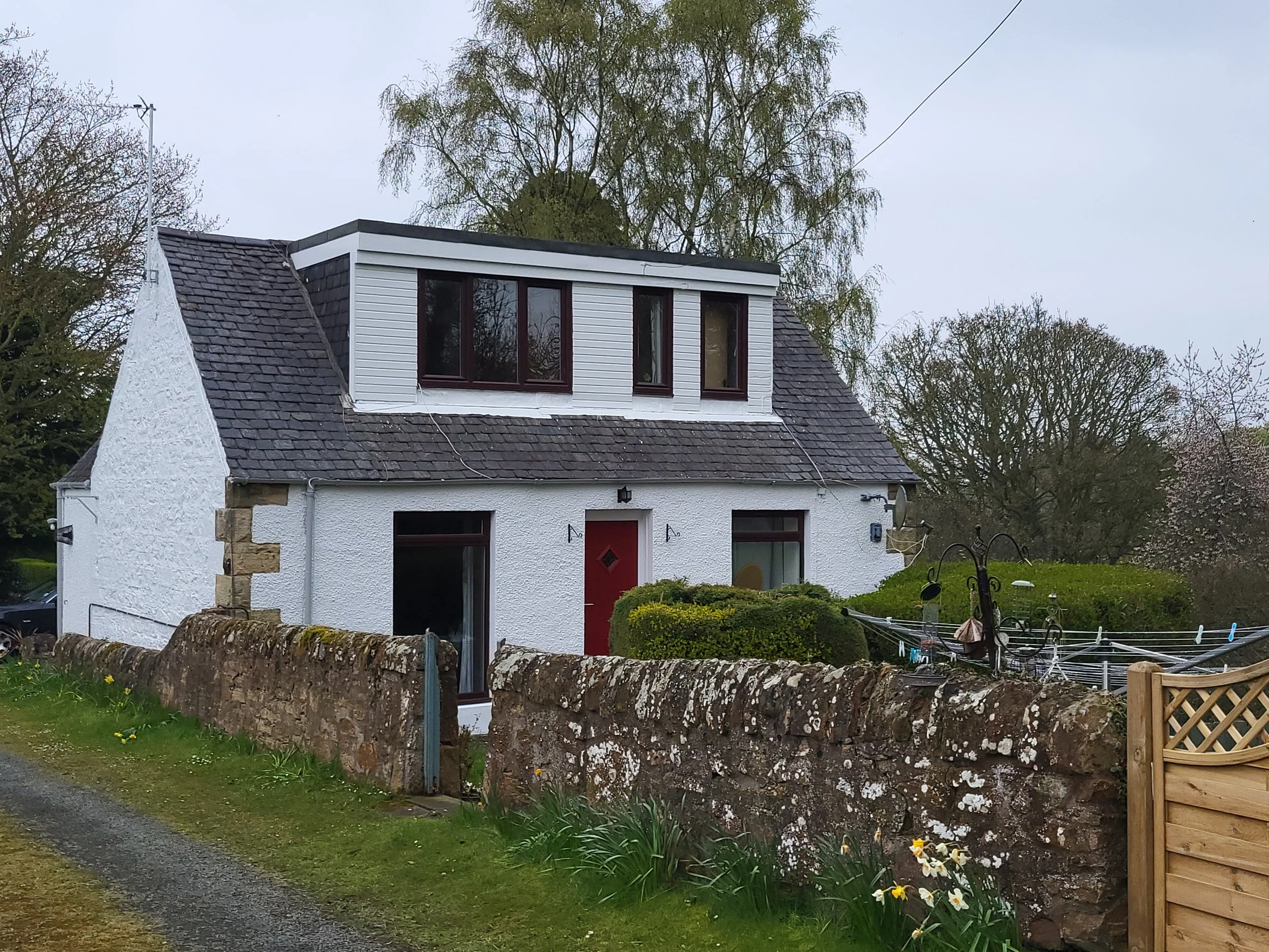 White cottage with dormer windows and red door 