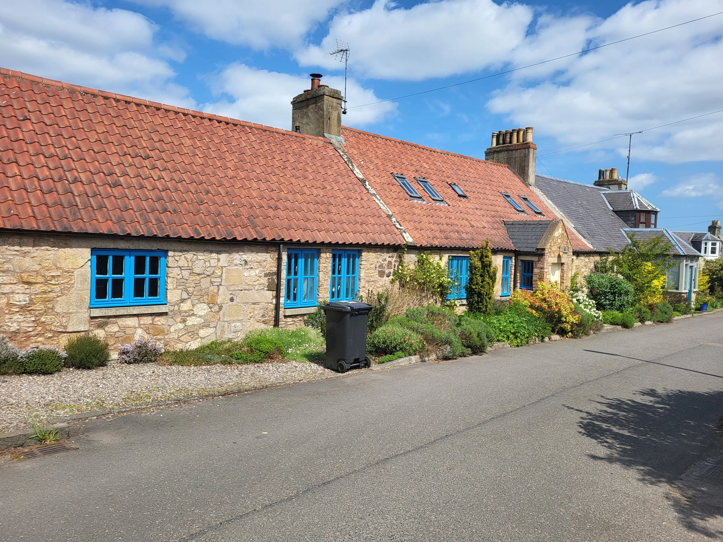 Cottage with stone exterior, red tiled roof, and blue framed windows on a quiet street.