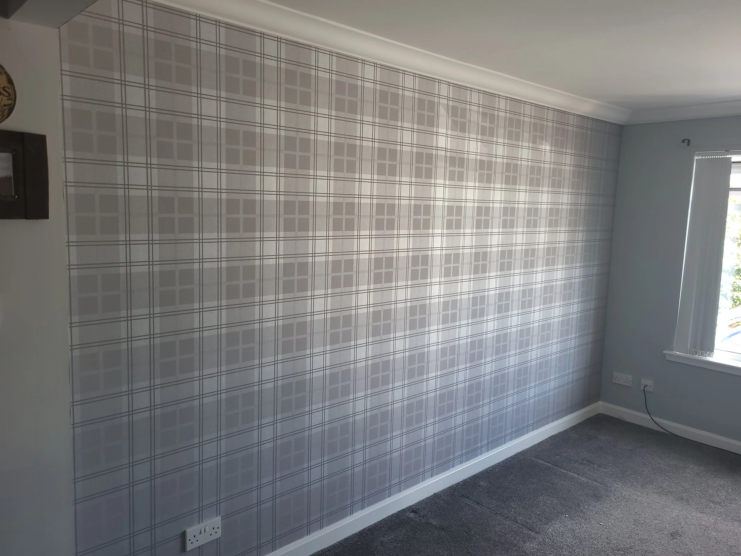 Empty room with plaid patterned wallpaper, gray carpet, and a window with blinds.