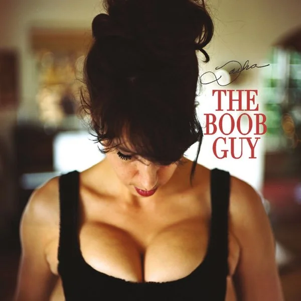 Woman with dark hair looking down, wearing a black top, with the words 'Tasha the Boob Guy' in red and black text beside her.
