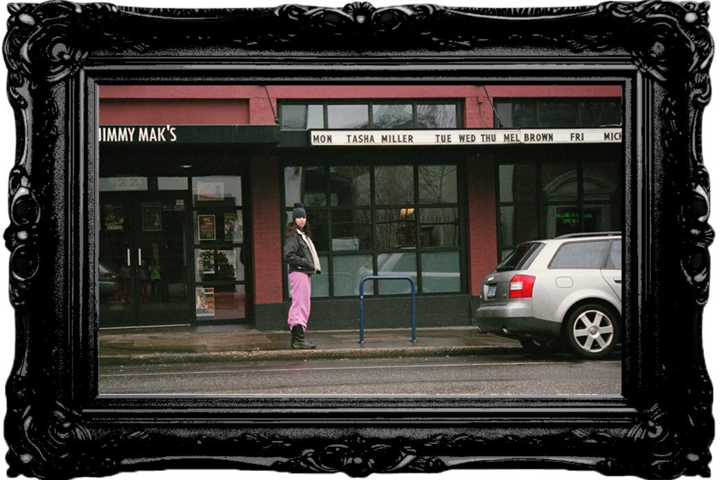 A woman standing on a wet sidewalk in front of a building with a sign reading 'Jimmy Mak's.' She wears a black jacket, pink pants, and a blue beanie. A white SUV is parked on the street beside her.