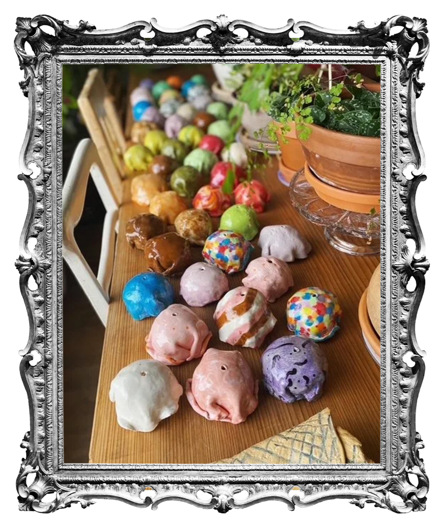 A collection of colorful, decorated cakes shaped like pigs, arranged on a wooden table with potted plants nearby.