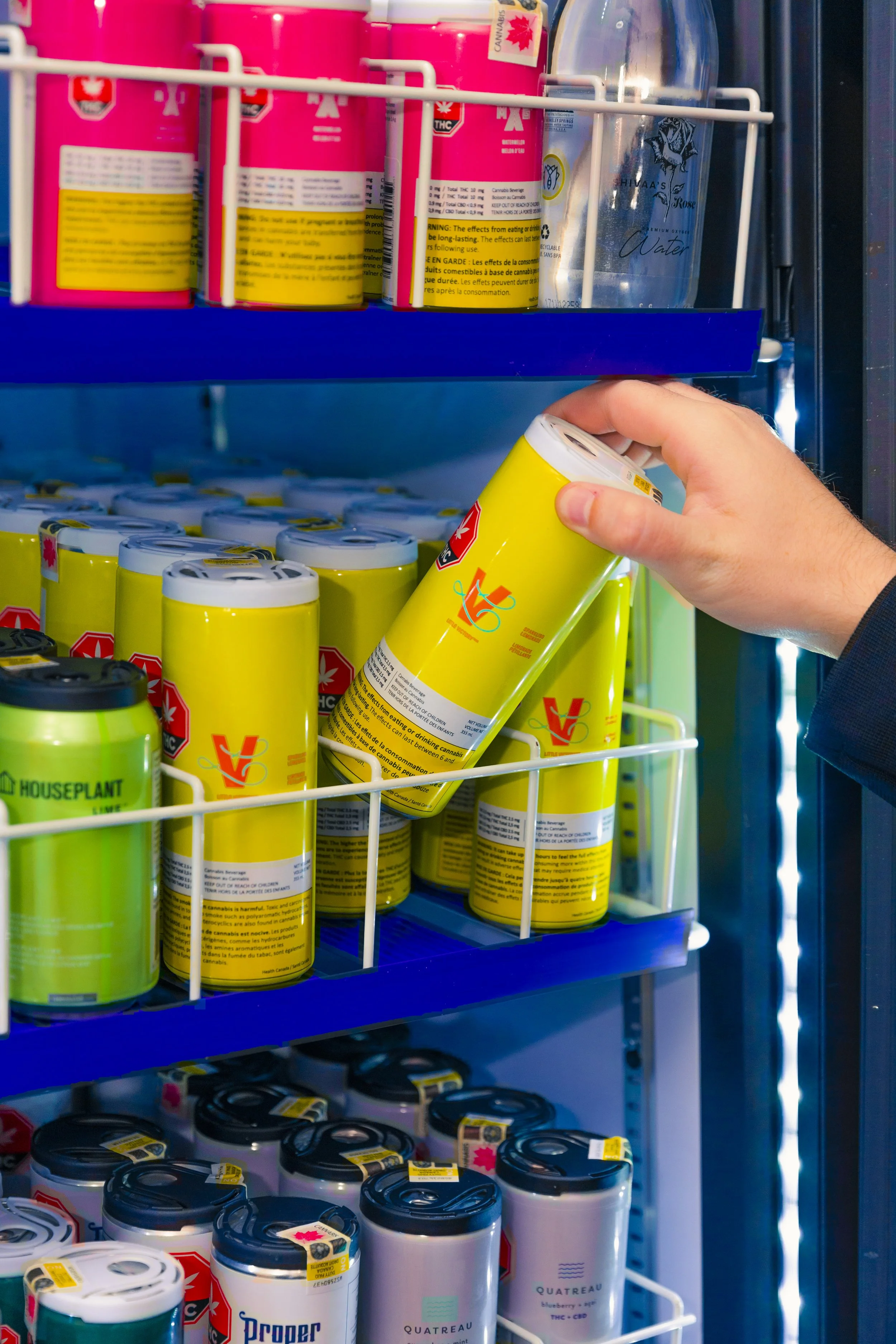 A person reaching into a vending machine and grabbing a yellow can labeled with cannabis warning.