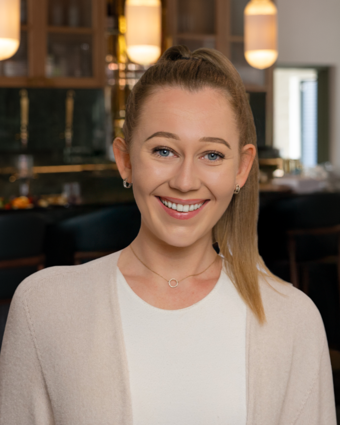 Mattie Hansing, a woman with blonde hair in a high ponytail smiling indoors with warm lighting.