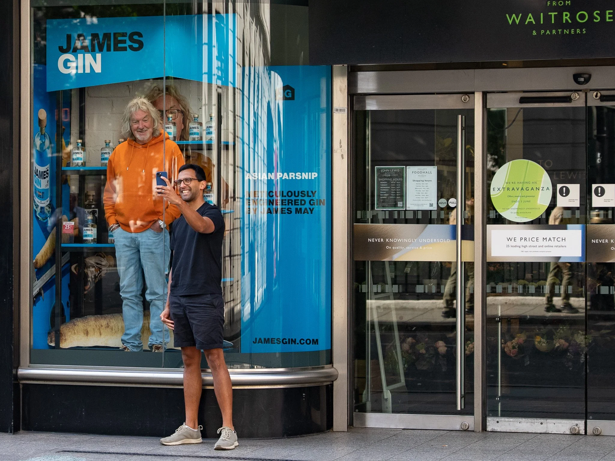 James May standing inside a waitrose john lewis store window. Surrounded by bottles of James Gin. James May