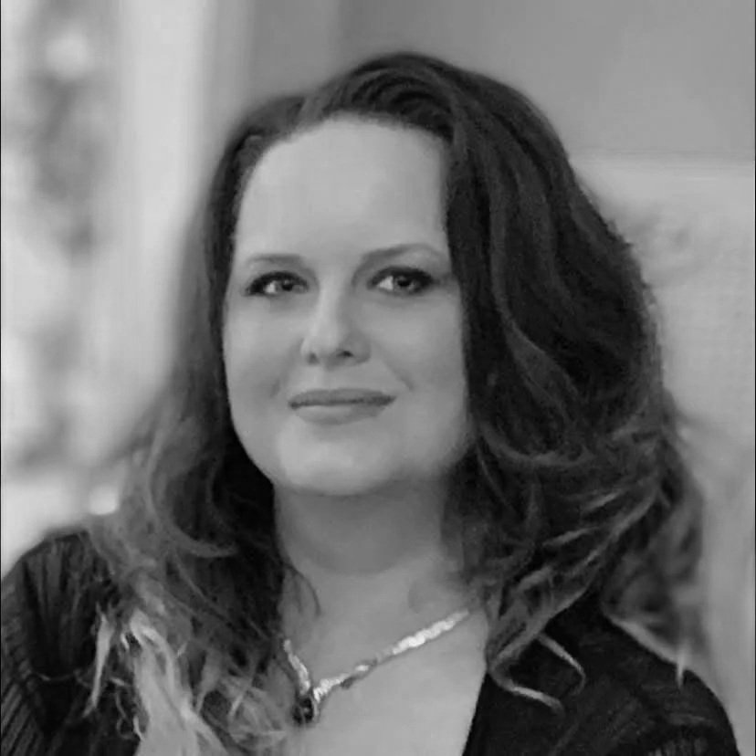 A smiling woman with dark, curly hair wearing a pearl necklace.