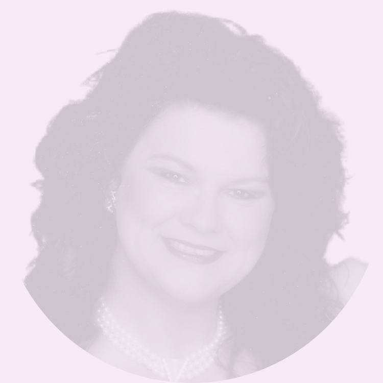 A woman with dark, voluminous curly hair smiling, wearing pearl earrings and a pearl necklace.
