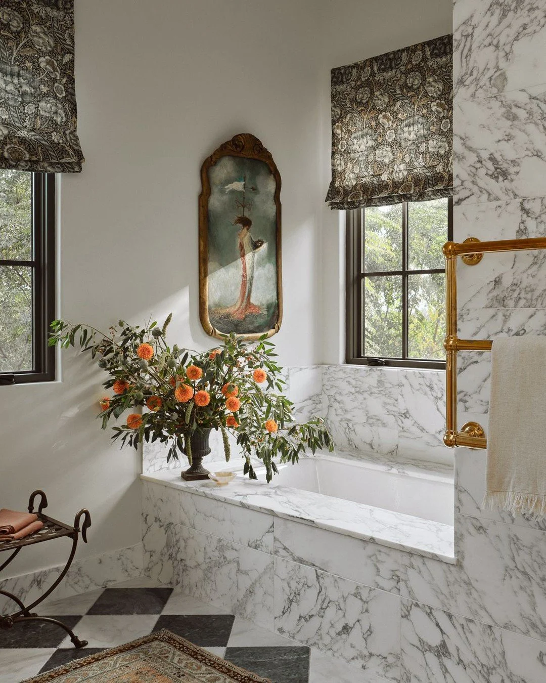 Elegant Arabescato Marble surrounds the mirrors, beaded white oak drawer fronts catch the light, and a reclaimed antique marble checkerboard floor grounds the room. A custom leaded-glass window adds artistry to the shower, while an antique art piece 