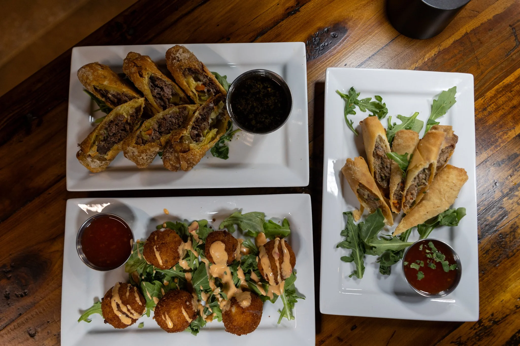 A photo of three different dishes The Club offers, drizzled with spicy mayo and served with greens and sauce. The Club is a great place to dine and is located in Lemont, Illinois.